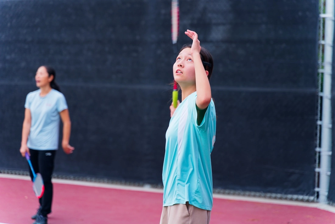 A coach watching closely as a player prepares an overhead shot